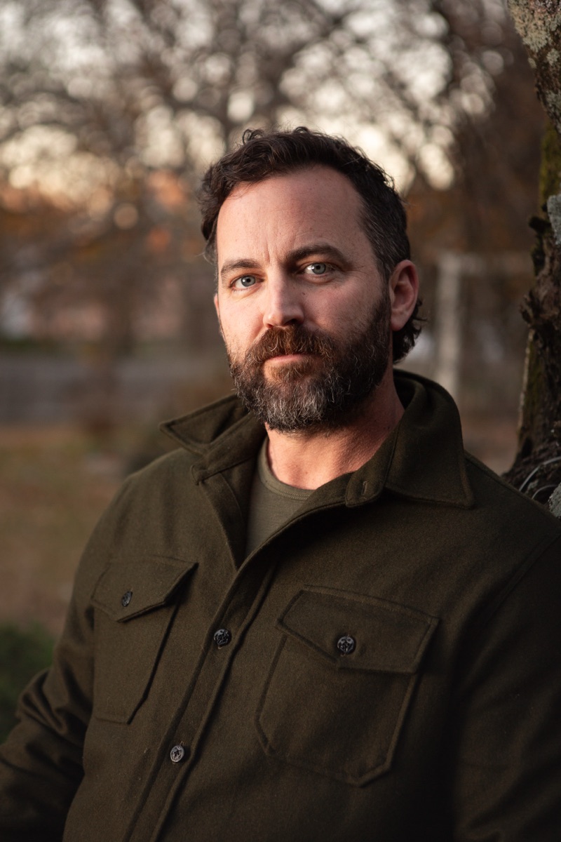 Robert Wilson Smith, actor, headshot outdoors in an olive overshirt among bare winter trees