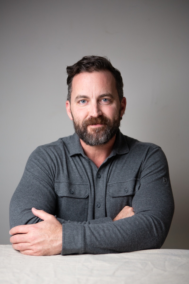Robert Wilson Smith, actor, studio headshot in a gray button shirt, arms folded, against a gray wall